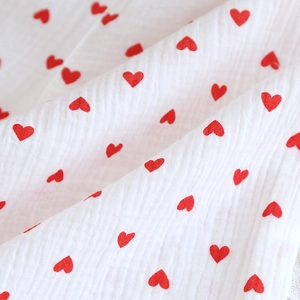 Close-up of soft breathable white cotton gauze fabric with red heart pattern texture