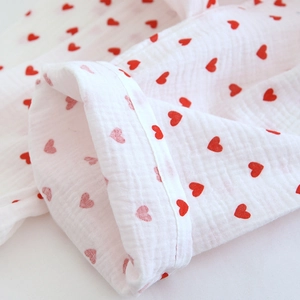 Close-up of white double gauze cotton fabric with red heart prints and neat seam detail