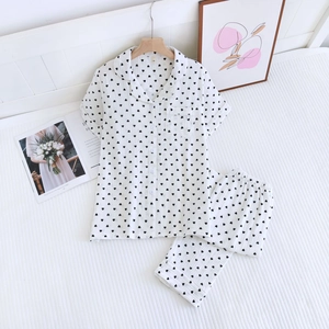 Détail d'un pyjama court en coton blanc à motif cœur noir sur une literie à rayures