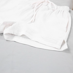 Detail of white double-layer cotton gauze shorts featuring drawstring elastic waist and side slits