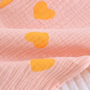 Gros plan d'un pyjama en coton crêpé rose avec motif cœurs jaunes et texture douce
