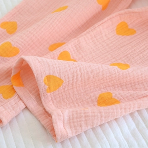 Gros plan sur du tissu de coton crépon rose avec motifs cœurs orange et texture douce