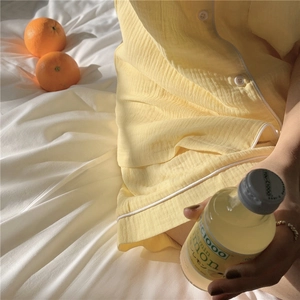 Detail of light yellow crepe pajamas set with white piping on bed with fruit and drinks