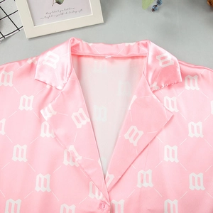 Close-up of pink satin shirt with gothic M-letter print and smooth silk texture