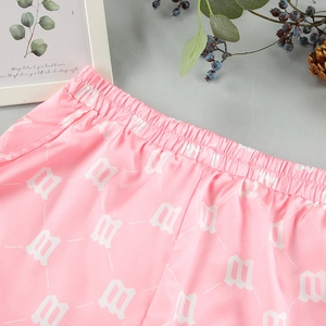 Detailed view of pink silk lounge shorts with elastic waist and white gothic M letter pattern