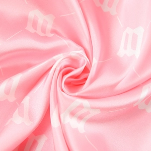 Detail of pink satin fabric with white gothic letter print and smooth glossy texture