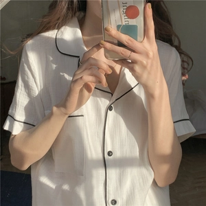 Detail of white cotton gauze pajama top with black piping, lapel, and front chest pocket