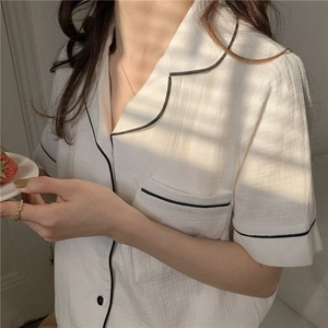 Detailed close-up of white gauze cotton pajama top with black contrast piping and pocket