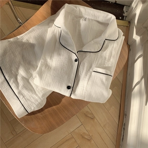 Detail of white cotton gauze pajamas with black piping laying on a rustic chair