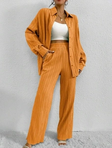 Detailed texture of orange pleated two-piece set featuring a long sleeve button-up shirt