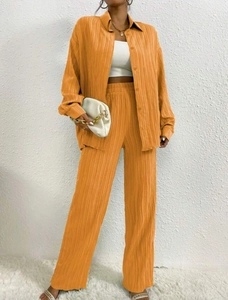 Detail of orange pleated fabric texture on loose shirt and wide-leg trousers set