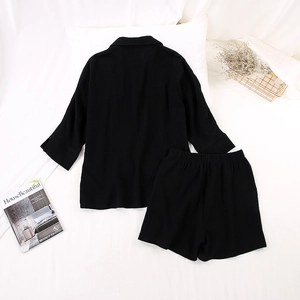 Flat lay of black cotton crepe pajama set with lapel shirt and drawstring shorts on white bed
