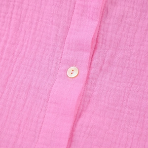 Macro detail of pink cotton crepe fabric showing the texture and yellow button closure