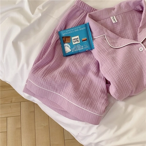 Detailed flat lay of purple gauze cotton pajama set with white piping on a bed