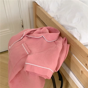 Detail of pink cotton gauze pajama top with white piping and lapel collar in a bedroom