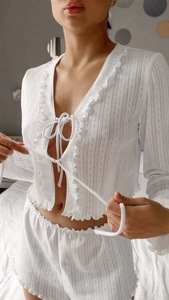 Detail of white pointelle knit pajamas featuring ruffled edges and delicate tie-front bows