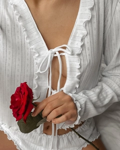 Detail of white hollowed-out knit pajamas set with delicate ruffles and lace-up ties