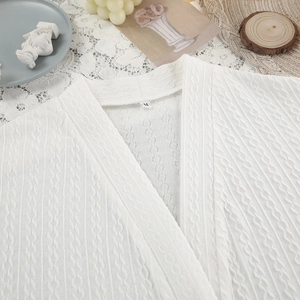 White cable knit cardigan with V-neck and soft fabric texture on a lace background