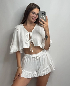 Detail view of white knitted two-piece loungewear with ruffle trim and lace-up front design