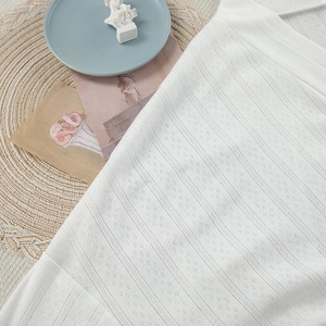Close-up of white pointelle knit fabric showing intricate diamond texture and soft material