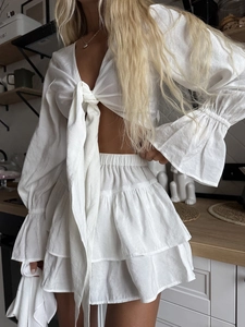 Detail of white ruffle trim long sleeve top and tiered skirt with delicate bow tie closure