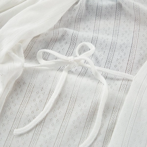 Close-up of white knit robe featuring vertical stripes, hollow texture, and tie-up bow detail