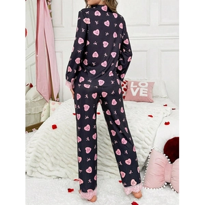 Women's black pajama set with pink heart prints and lace trim in a cozy bedroom setting