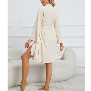 Women's cream waffle robe with pink piping and adjustable waist tie in an indoor setting