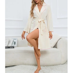 Elegant cream long-sleeved bathrobe with pink piping and tie-waist in a cozy indoor setting