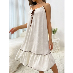 Close-up of white textured slip dress with brown bow tie detail and ruffled hemline
