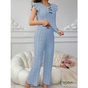 Two-piece light blue pajama set with bow details and lace texture in a cozy room setting