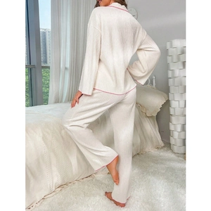 Two-piece cream plissé pajama set with pink contrast piping in a cozy bedroom setting