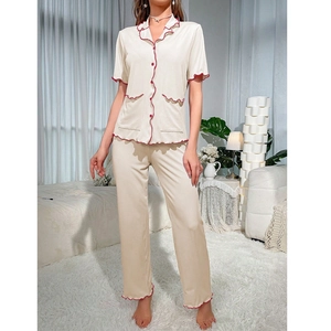 Close-up of contrast red wavy trim on beige short-sleeved pajama top with buttons