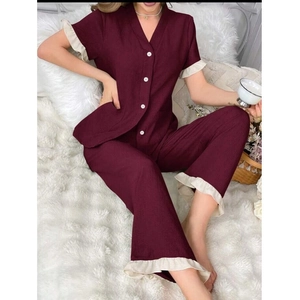 Détail d'un pyjama rouge à col en V avec des volants beiges et des boutons blancs sur la manche