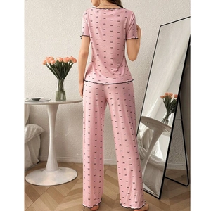 Pink two-piece pajama set with black bow print and lettuce edge trim in a home setting