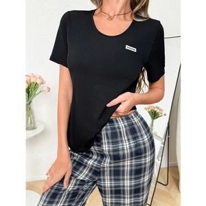 Détail d'un t-shirt noir avec étiquette design et d'un pantalon de pyjama à carreaux bleu