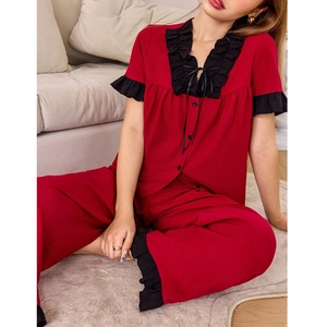 Detail of red pajama set with black lace trim, V-neck, and bow decoration on fabric