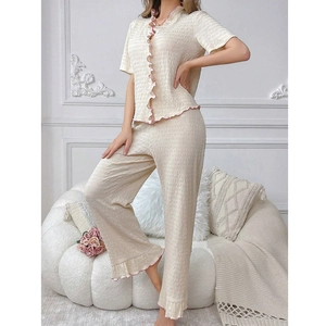 Close-up of cream textured pajamas set with pink ruffle edges in a cozy room