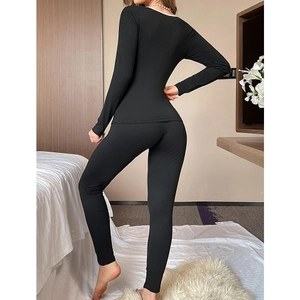 Women's slim black pajama set with white contrast piping and long pants in a bedroom scene