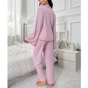 Pink maternity pajama set with long sleeves and red piping trim in a bright bedroom setting