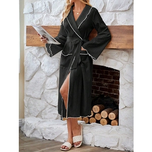 Detail of black long-sleeved robe with white wavy trim and belted waist in home setting
