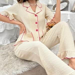 Women's chic two-piece seersucker pajama set with pink trim in a cozy bedroom