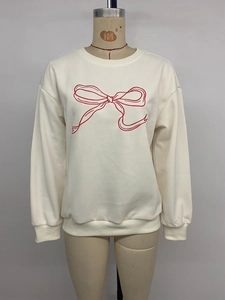 Close-up of red embroidered bow on a cream crewneck sweatshirt with ribbed cuffs