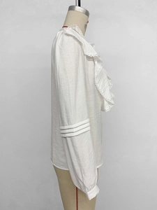 Detailed side view of white long sleeve shirt with ruffle trim and pleated sleeve texture