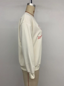 Detail of red embroidered bow on beige crewneck sweatshirt with ribbed cuff design