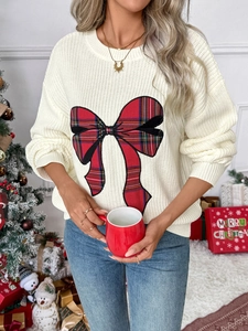 Detail of knit sweater featuring a red tartan bow pattern against a festive Christmas tree backdrop