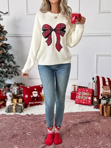 Detail of white knit sweater featuring a festive red plaid bow applique for winter