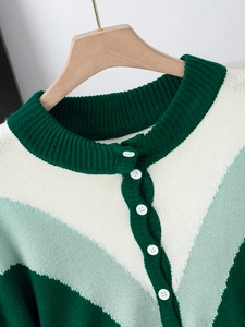 Green and white color-block knitted cardigan with white buttons on a wooden hanger