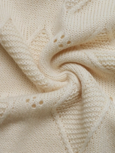 Macro shot of off-white pointelle knit fabric with delicate diamond hollow patterns