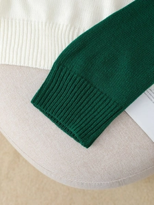 Close-up of color-block knit sweater with dark green ribbed cuffs and cream knit fabric